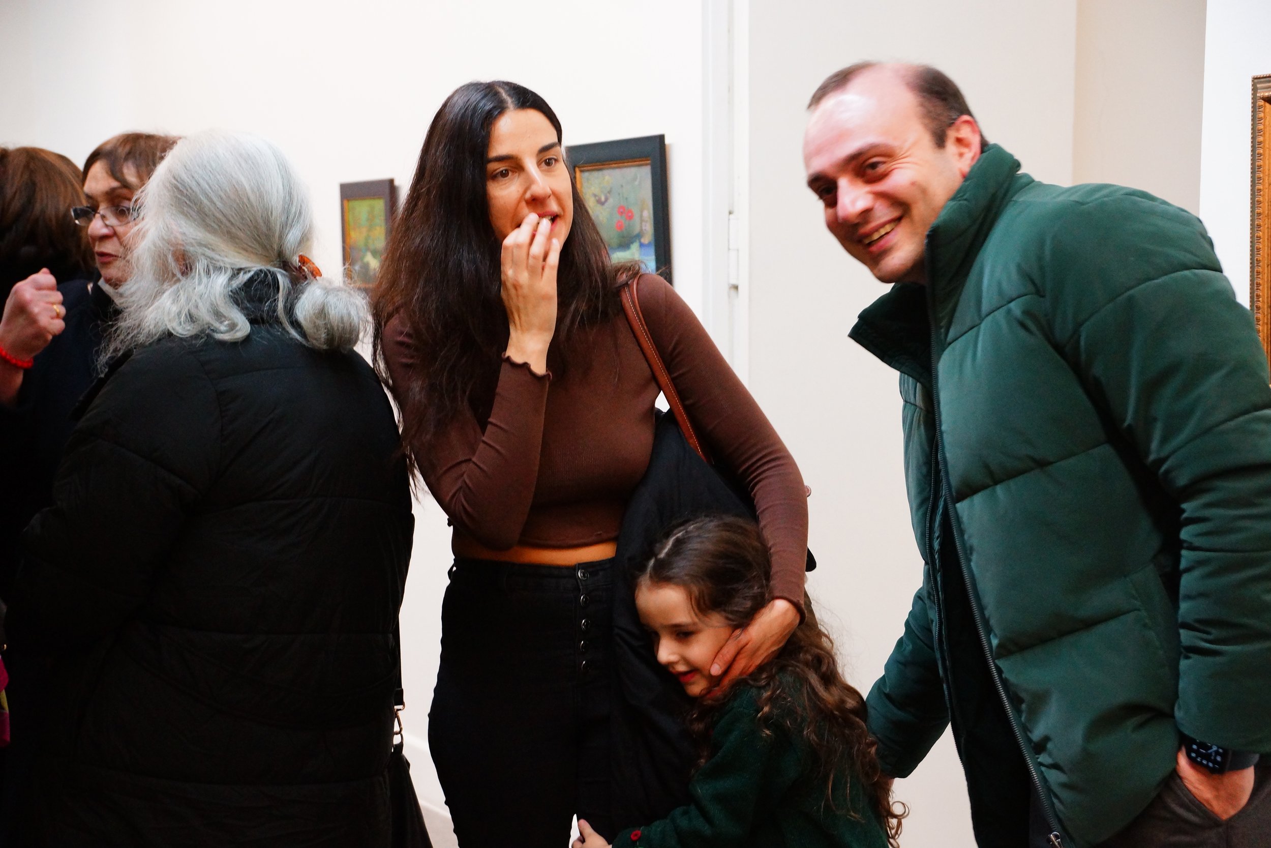 Group of people conversing at an art gallery, including a woman, a man, and a young girl.