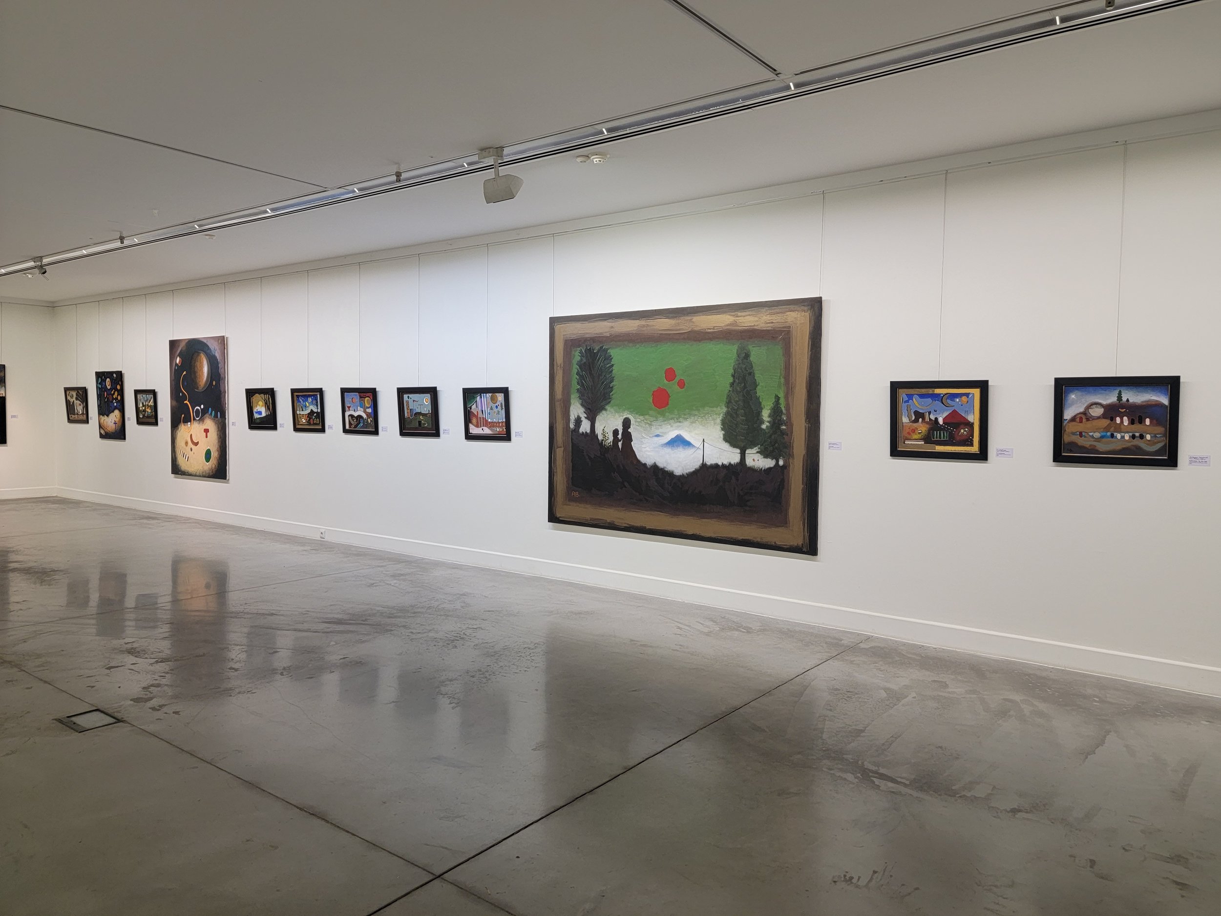 A gallery wall displaying various framed paintings with one large landscape painting in the center and smaller paintings surrounding it.