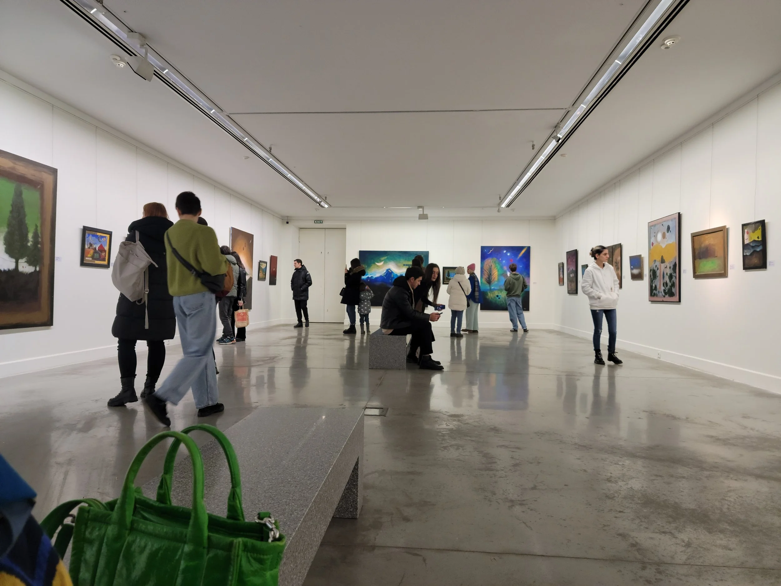 People viewing artwork in a well-lit art gallery with white walls and gray flooring.