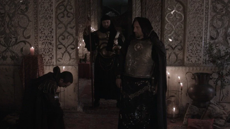 Vizier Beka Goshadze, kneeling, informs the king that his wife has been unfaithful. Warrior Nikoloz Kobalava watches the vizier with suspicion, while the emperor proceeds toward the queen’s chamber.