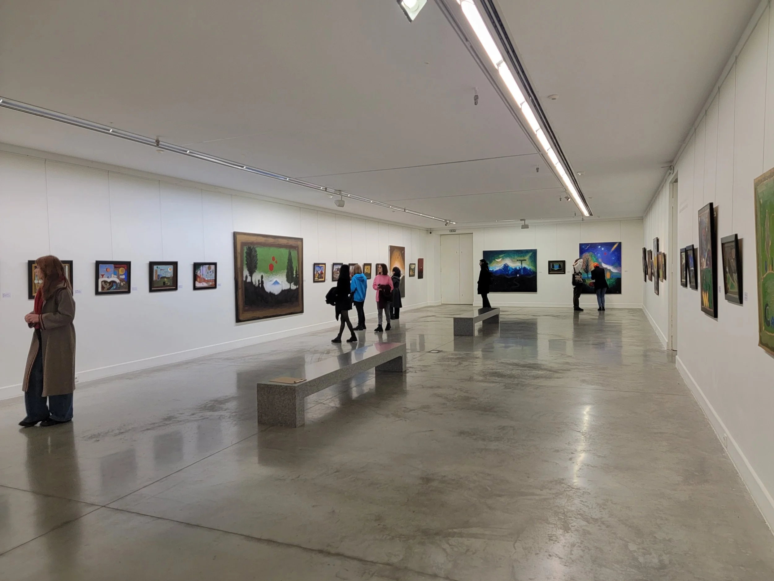 People viewing various paintings displayed on white gallery walls in an art museum.