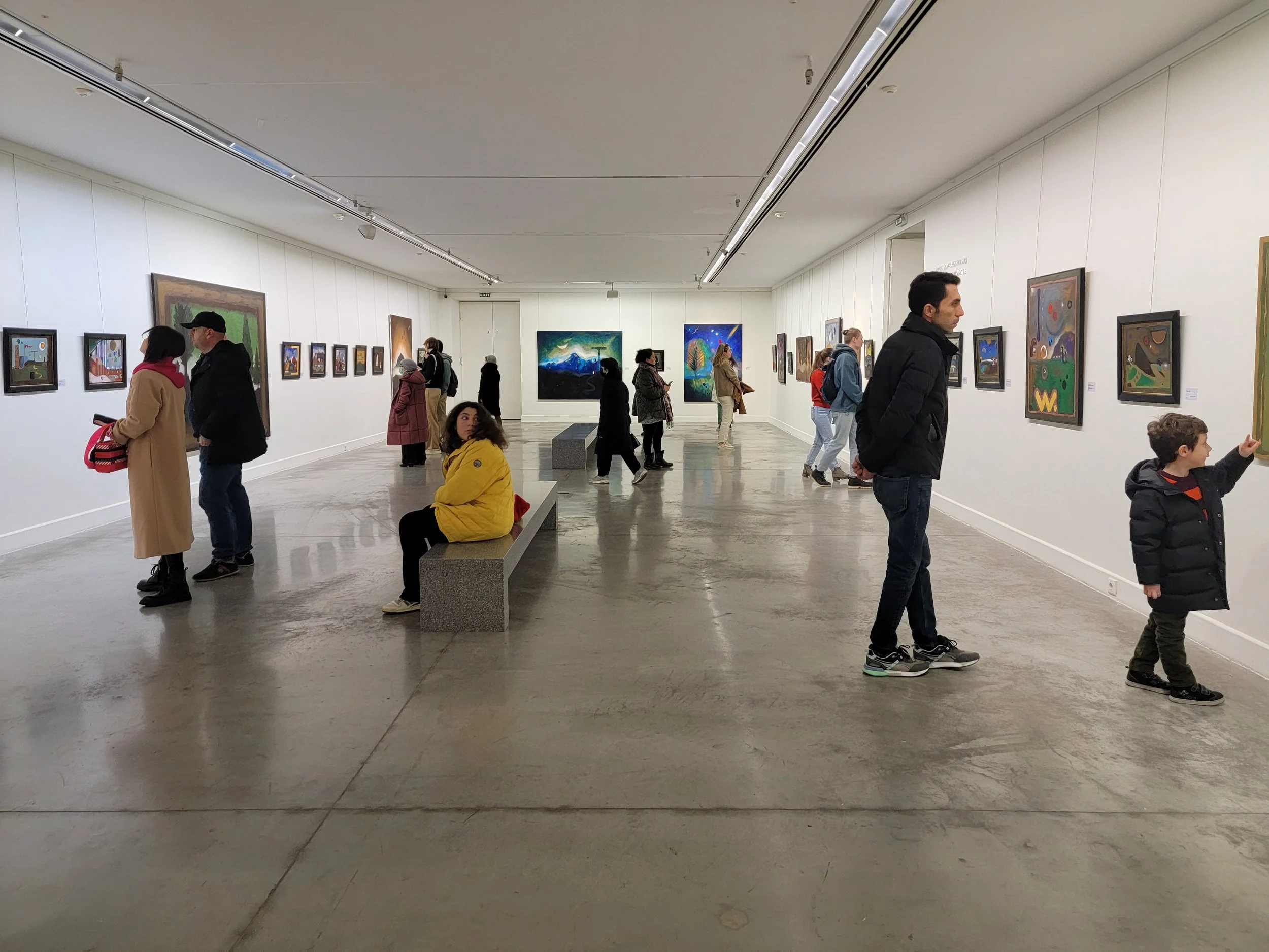 People viewing artwork in an art gallery with white walls and a concrete floor.