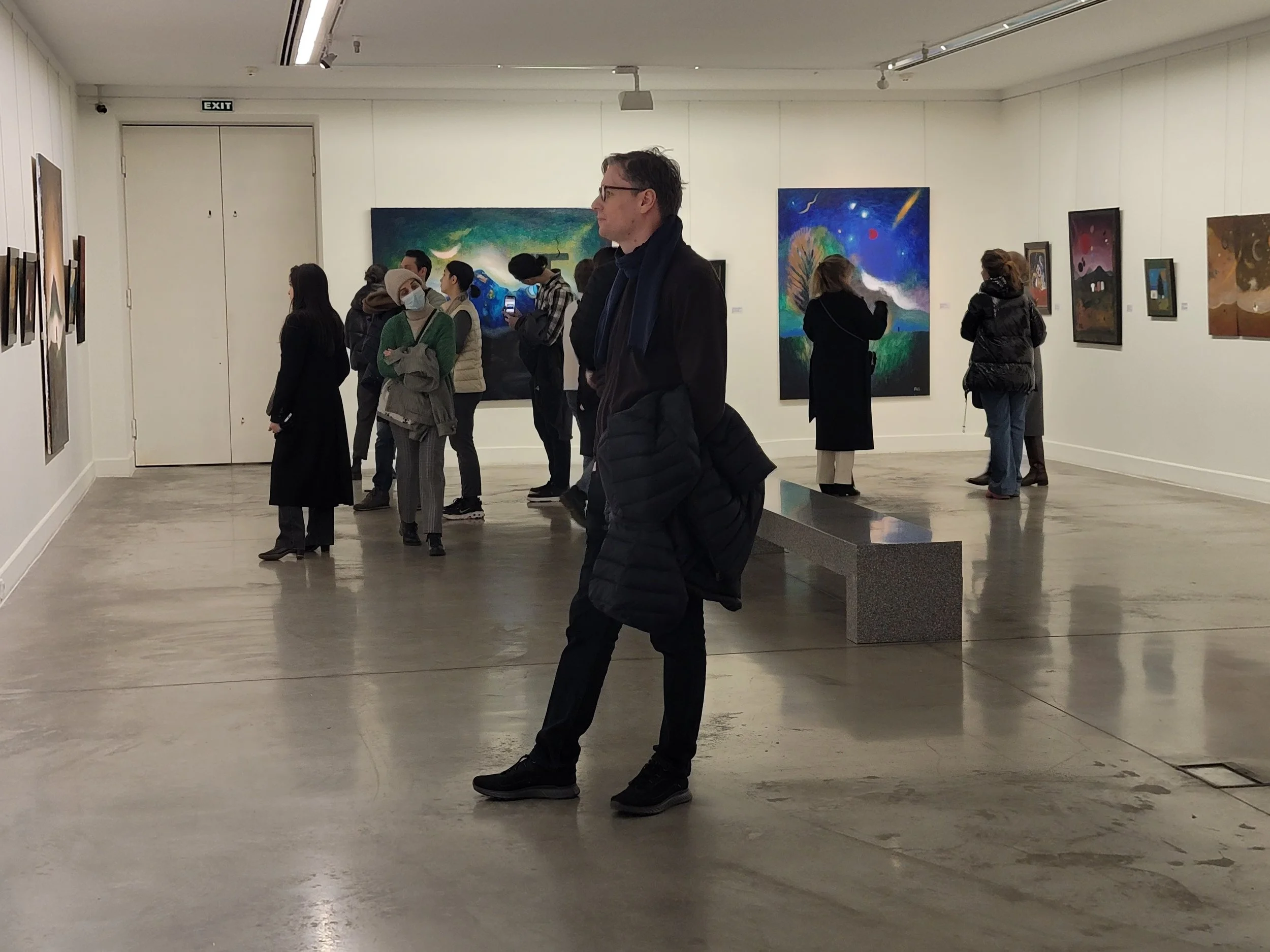 People viewing art paintings in an art gallery with white walls and concrete floor.
