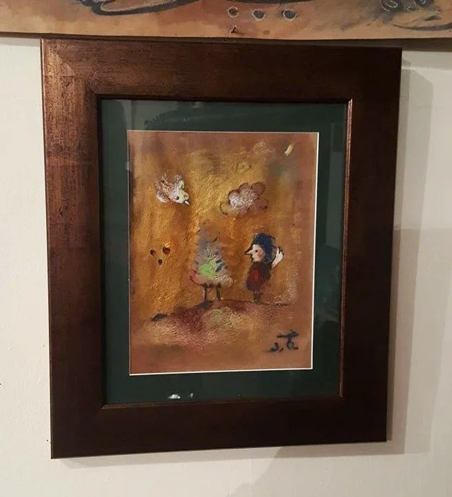 Framed abstract painting of two figures facing each other with a cloudy sky above, rendered in warm earth tones.