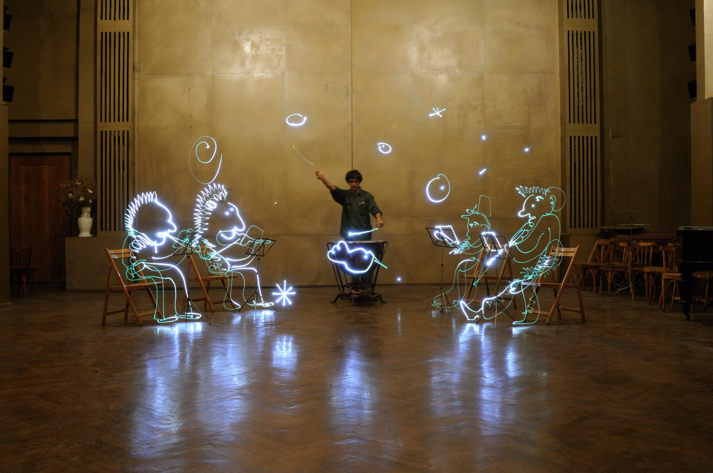 Anton Balanchivadze creates light drawings , freezlight, of cartoon-like characters of orchestra and stars, standing in center as conductor, on a long-exposure photo of Anton Sokolov