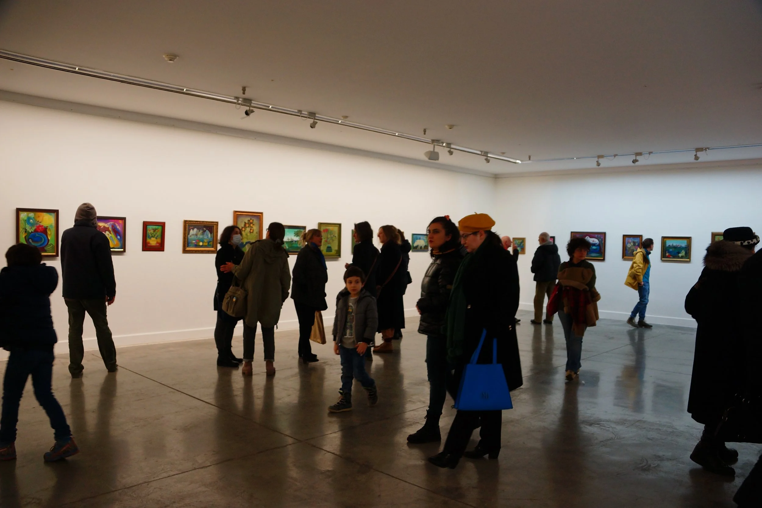 People observing colorful paintings in an art gallery.