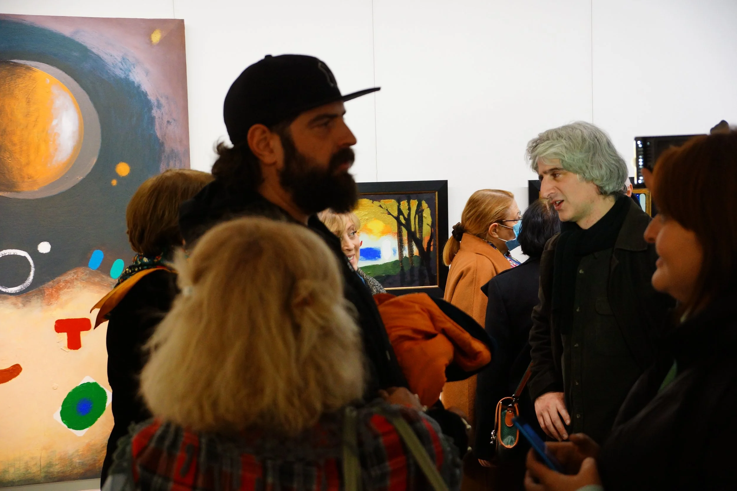 People talking and socializing at an art gallery, with colorful abstract paintings on the wall behind them.