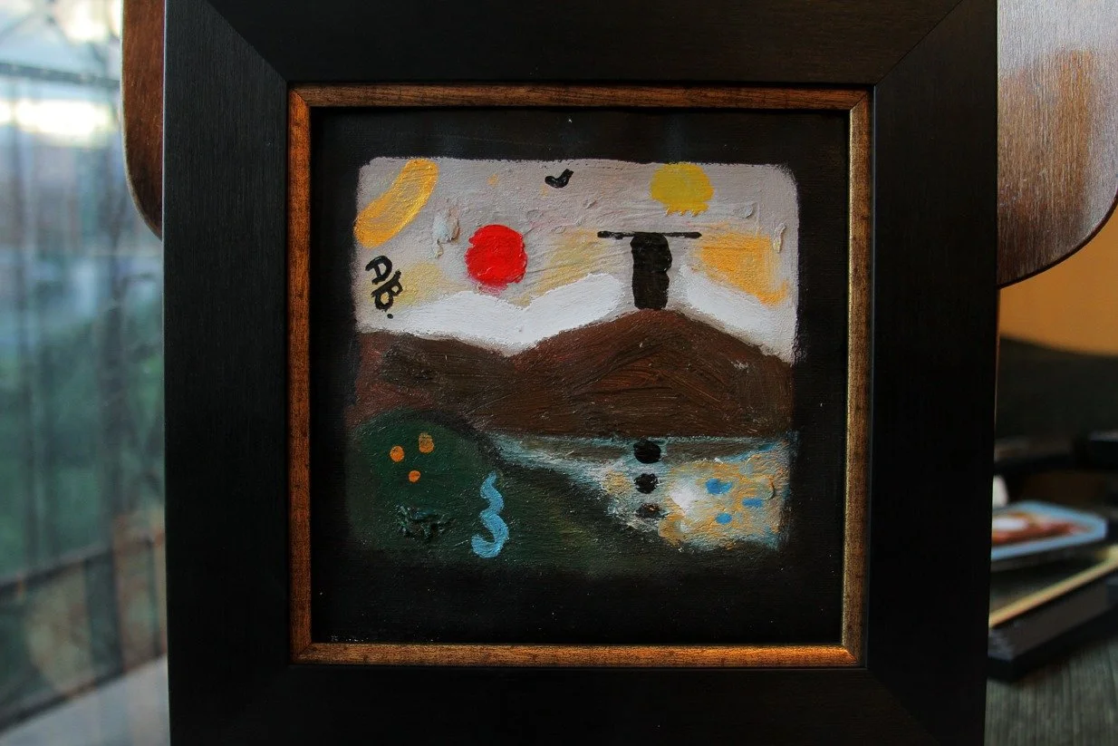 Abstract landscape painting with mountains, water, and sky, featuring a red sun, yellow sun, and black shapes, framed in black wood.