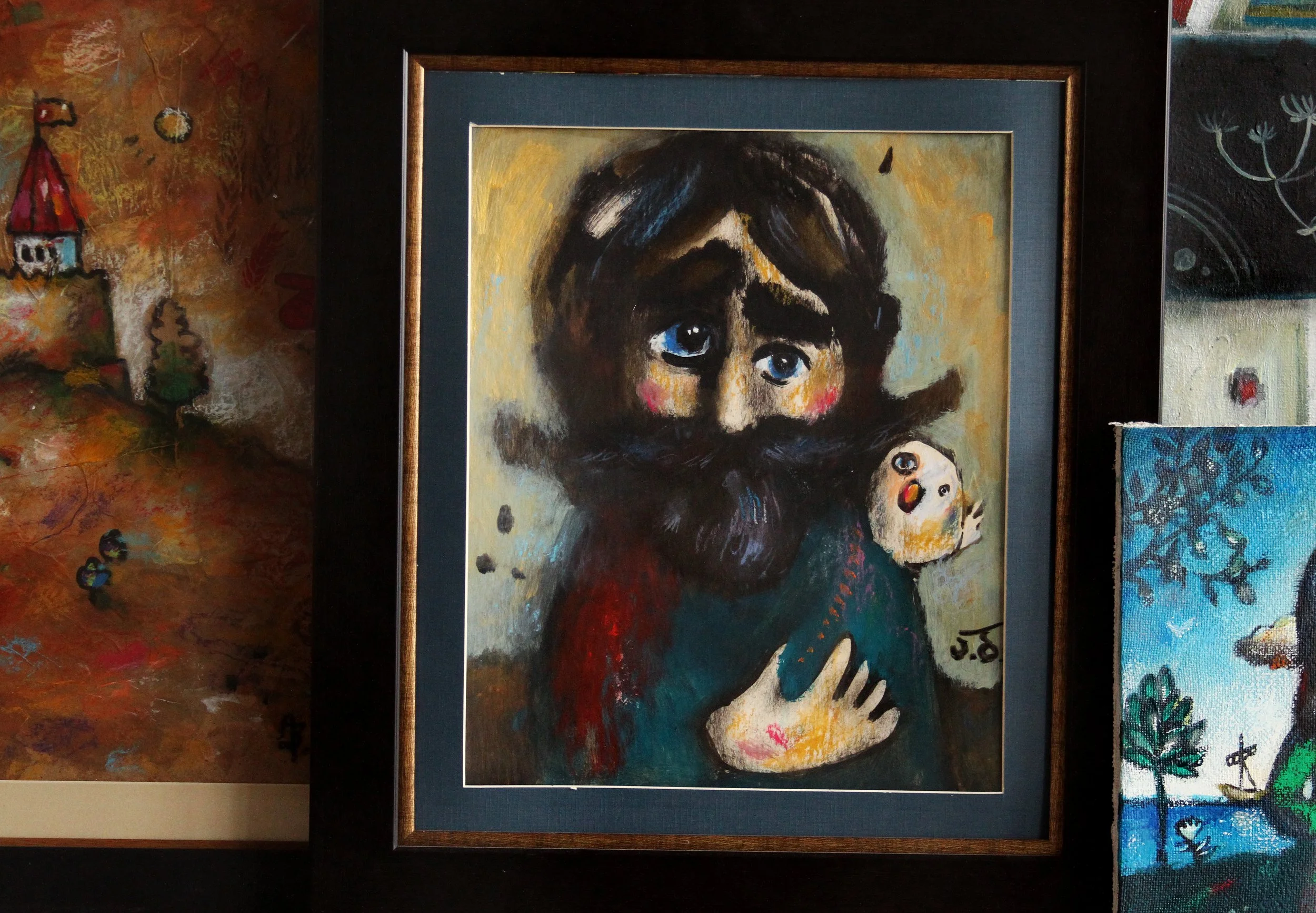 A colorful painting of a person with a large beard, large eyes, holding a small creature with a similar face, in a wooden frame.