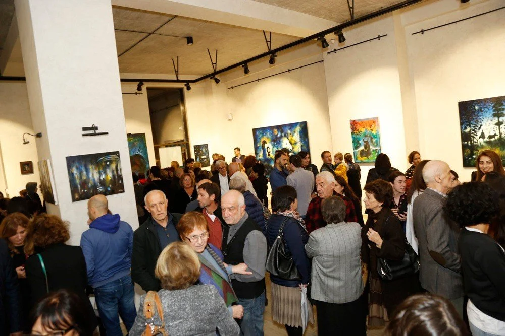 People attending an art gallery exhibit, viewing and discussing colorful paintings displayed on white walls.