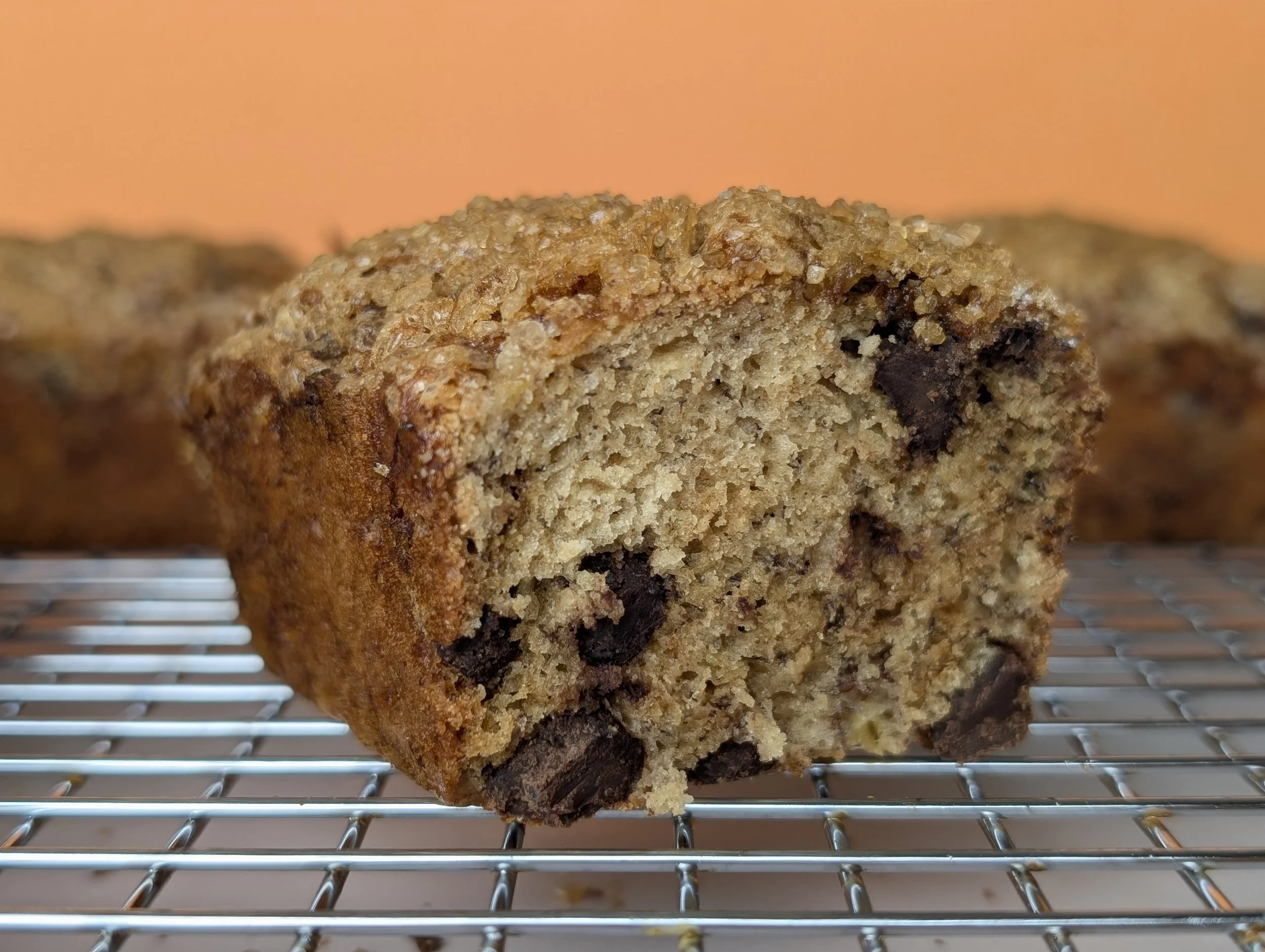 Close-up of a partially eaten mini banana chocolate chip loaf with a golden-brown crust on a wire cooling rack.