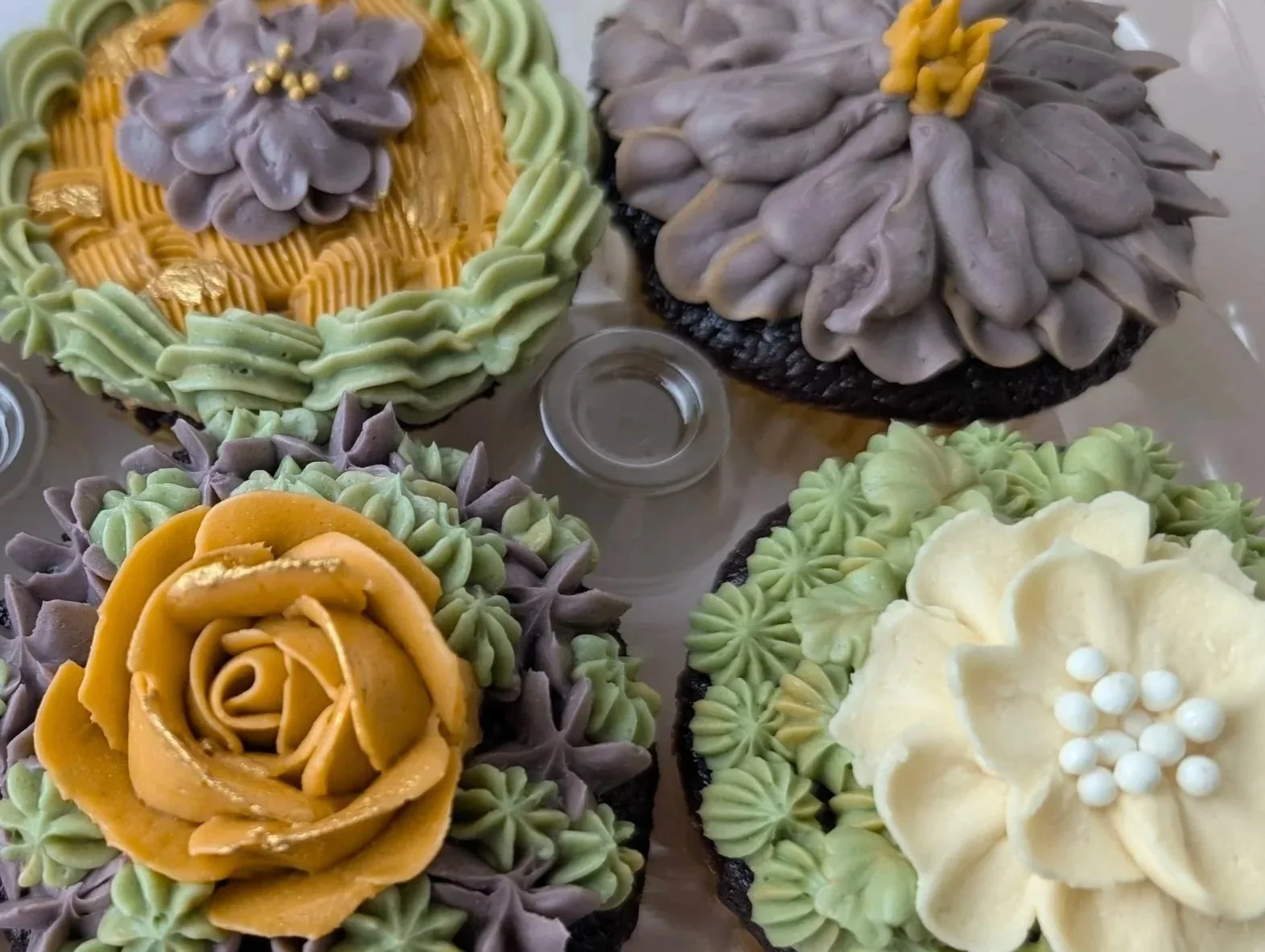 Decorative cupcakes with floral and piping designs in various colors such as yellow, purple, green, and white, featuring intricate frosting flowers and embellishments.