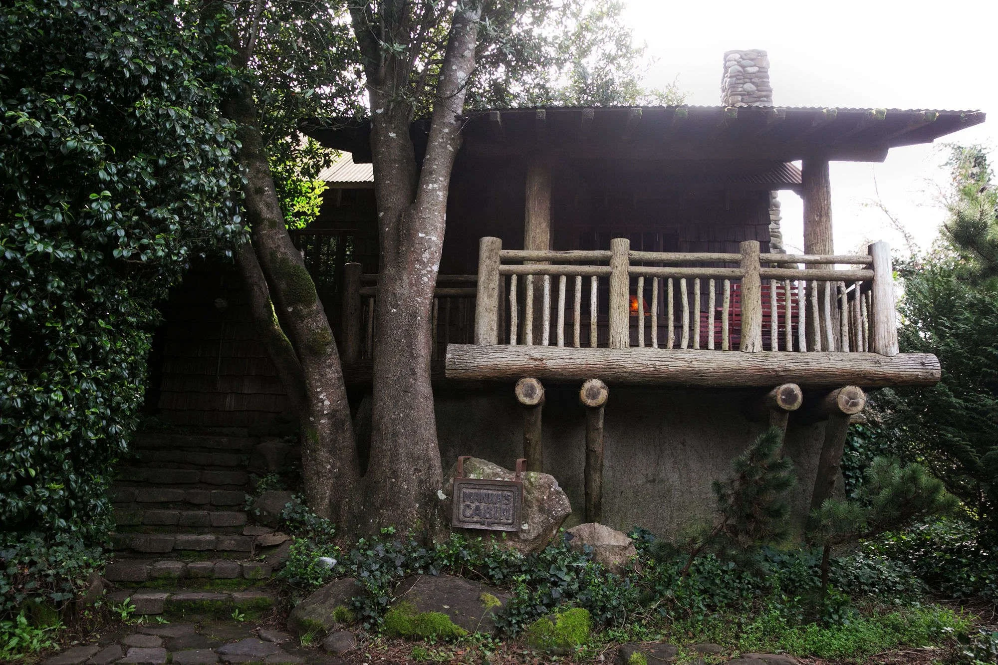 Treehouse with a wooden balcony, stone steps leading up to it, surrounded by greenery and a sign that says "Animals Cabin".