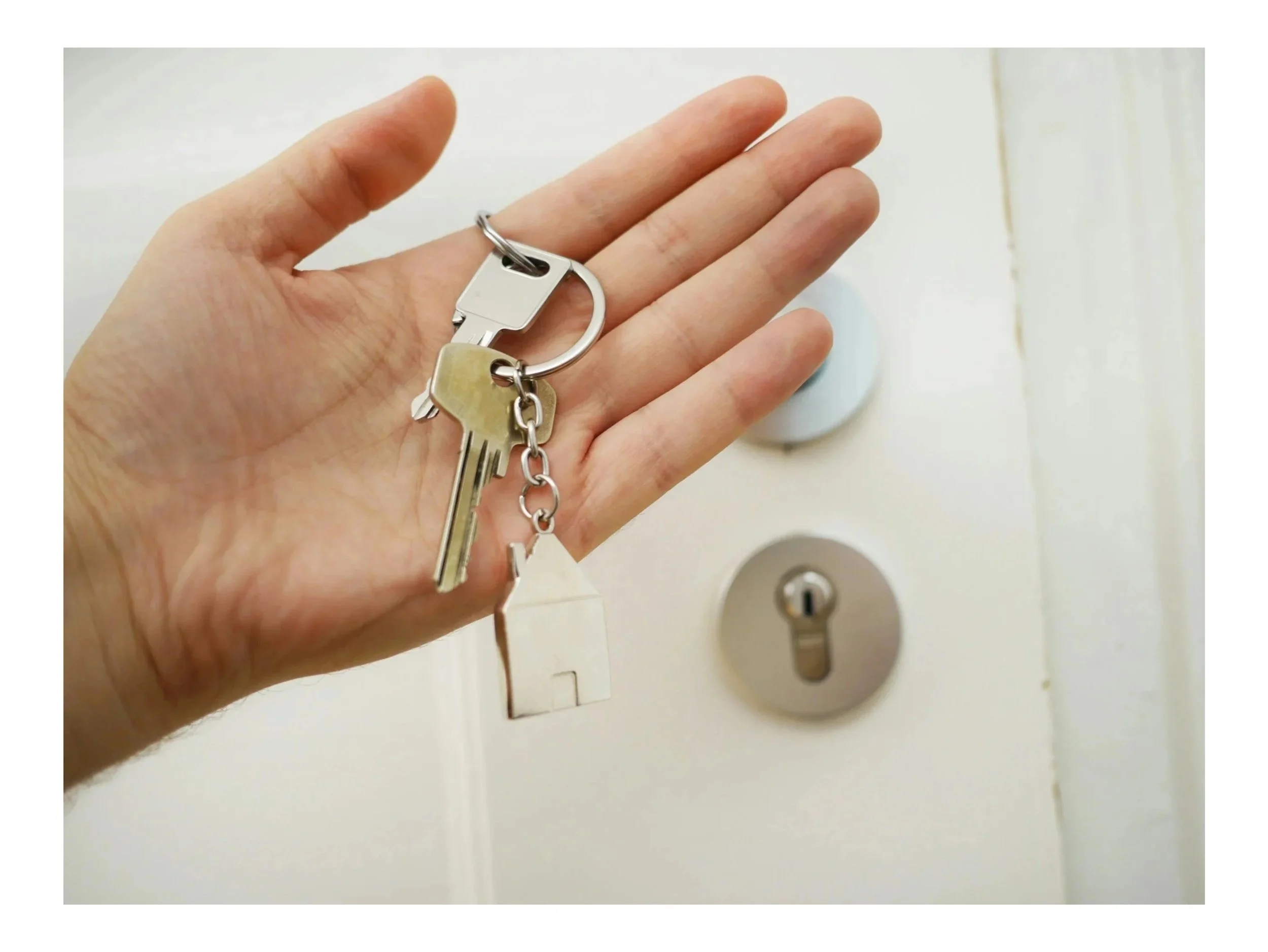 Close-up of a hand holding a keychain with keys near a deadbolt lock on a door.
