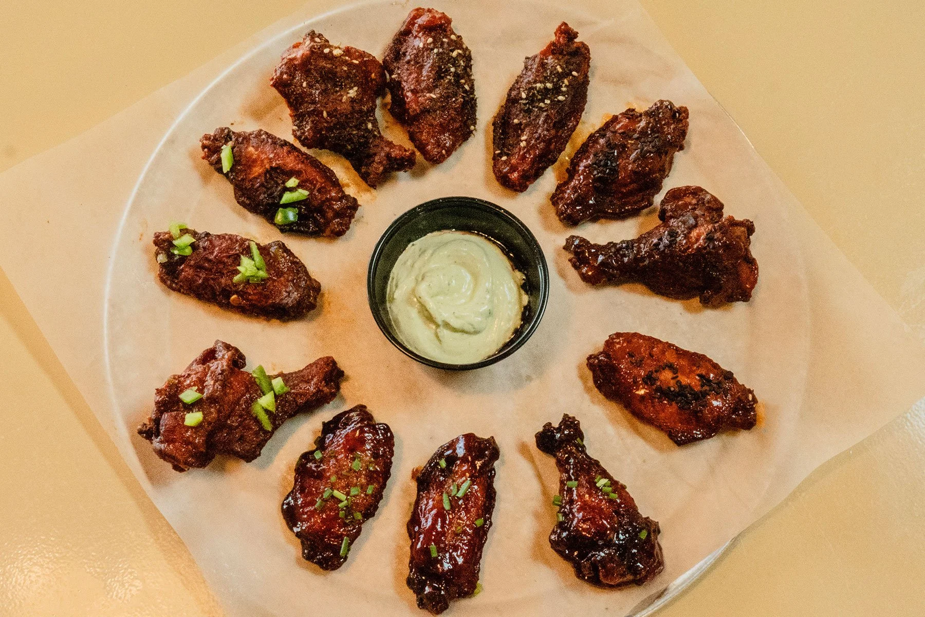 A round white plate with twelve buffalo chicken wings and a small cup of ranch dipping sauce in the center, garnished with chopped green onions.