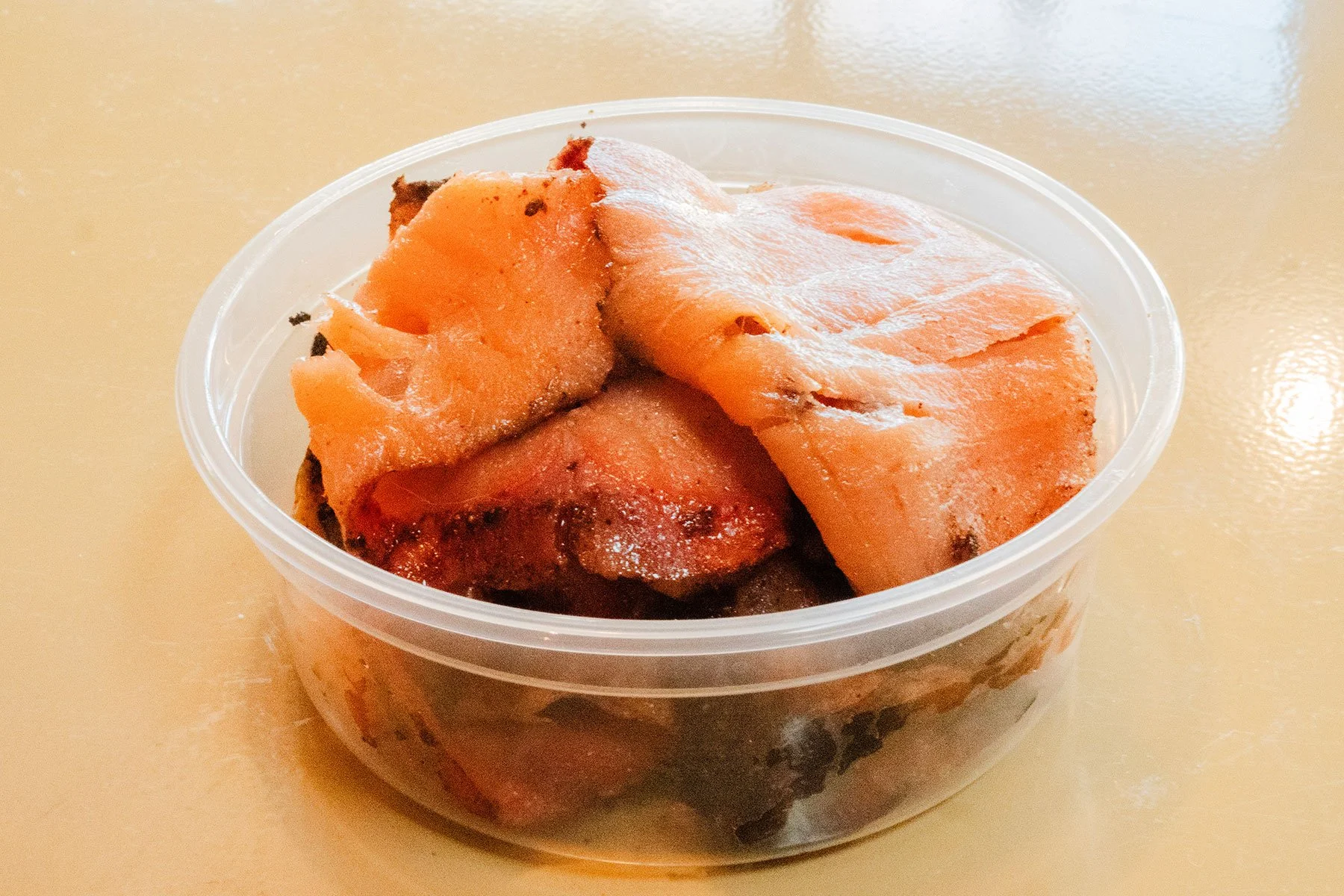 Close-up of frozen sweet potatoes in a clear plastic container on a beige surface.