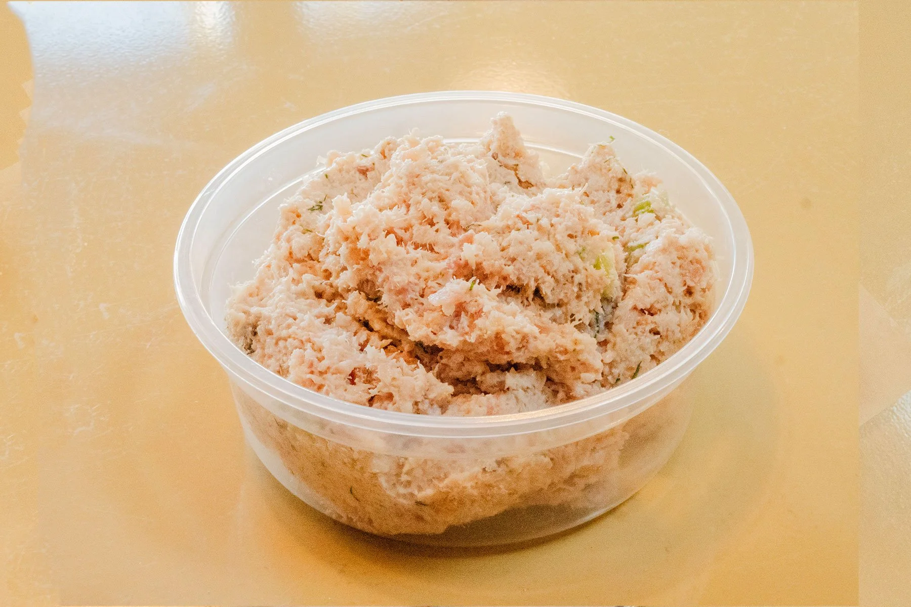 Close-up of a clear plastic container filled with shredded or chopped crab meat, on a beige surface.