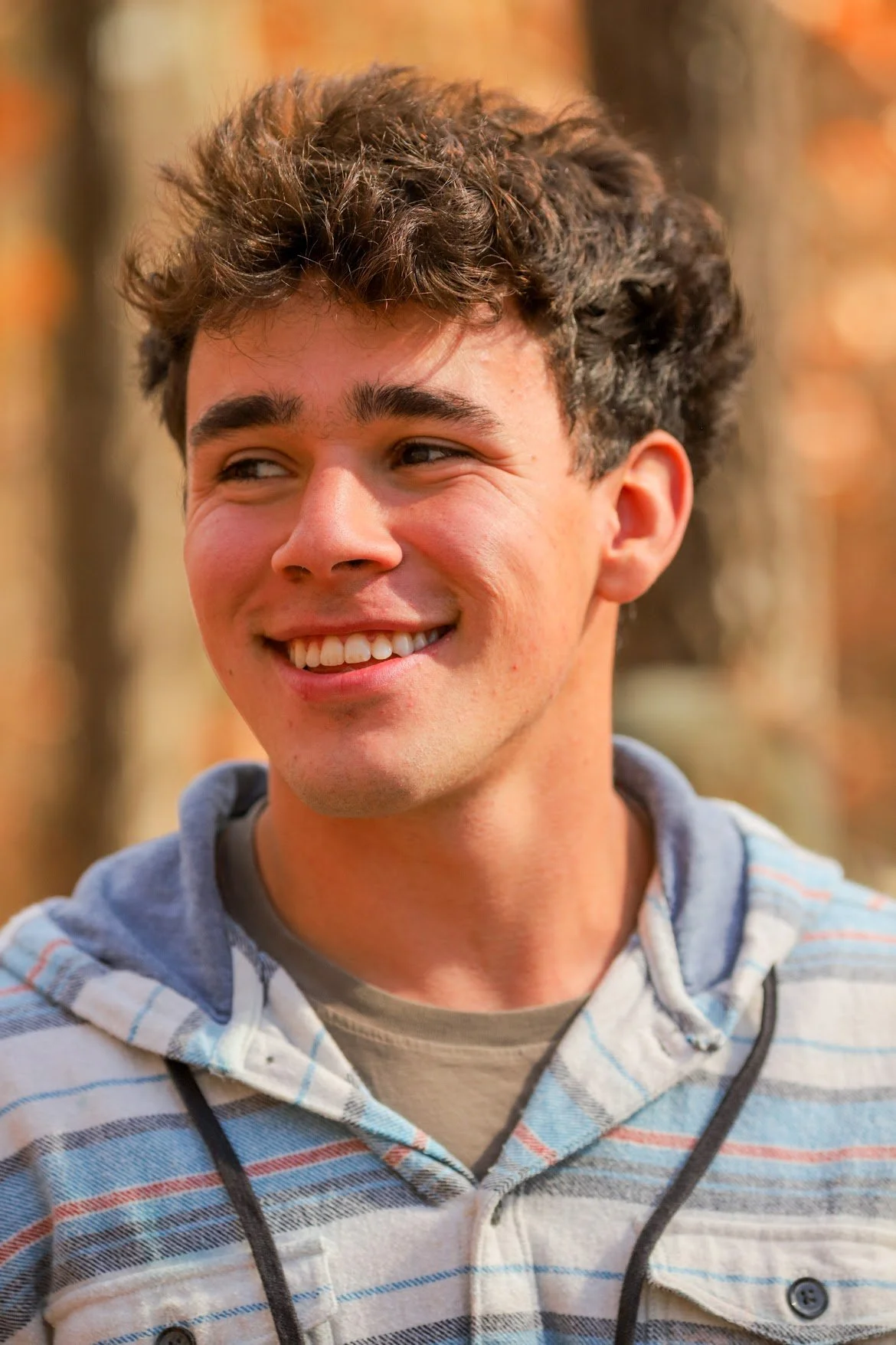 Young man smiling outdoors during autumn, wearing a striped hoodie with the hood down.