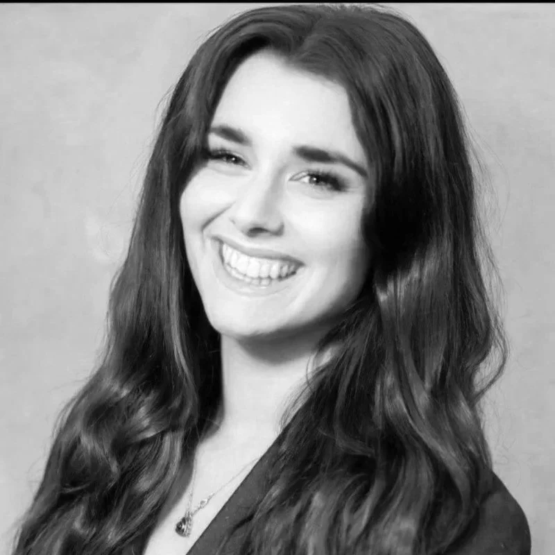 Black and white photo of a young woman with long wavy hair, smiling and showing her teeth.