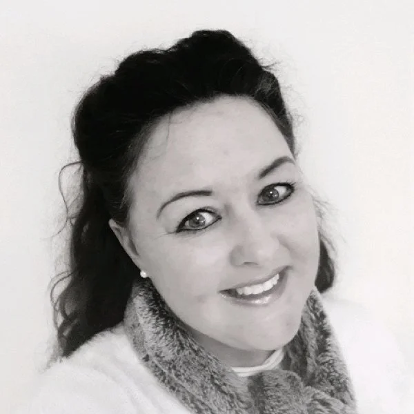 Black and white photo of a woman with dark hair, smiling, wearing earrings and a patterned scarf.