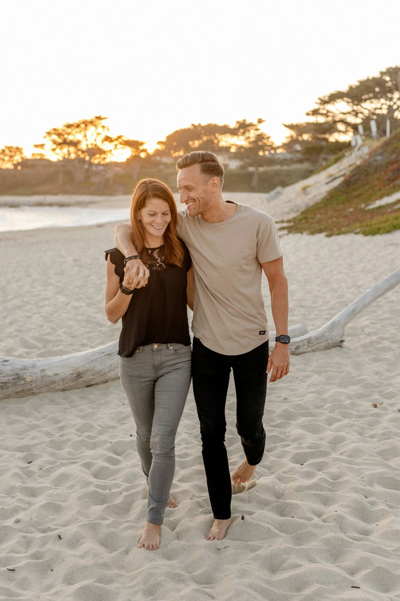 A couple walking barefoot on the beach during sunset, smiling and enjoying each other's company.