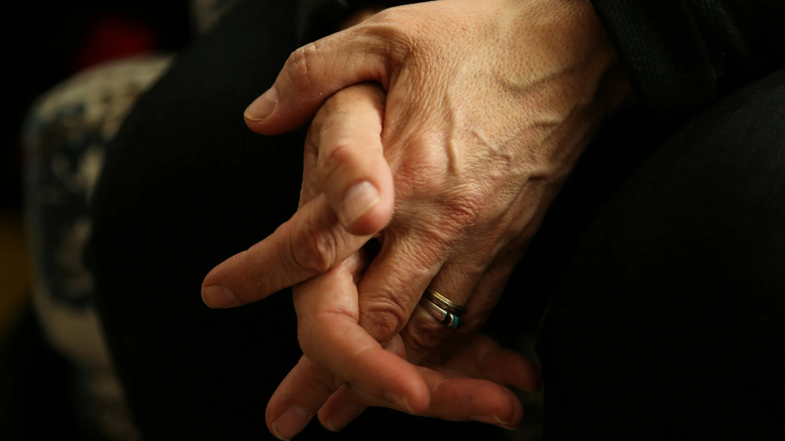 Close-up of two hands clasped together, one with a wedding ring.