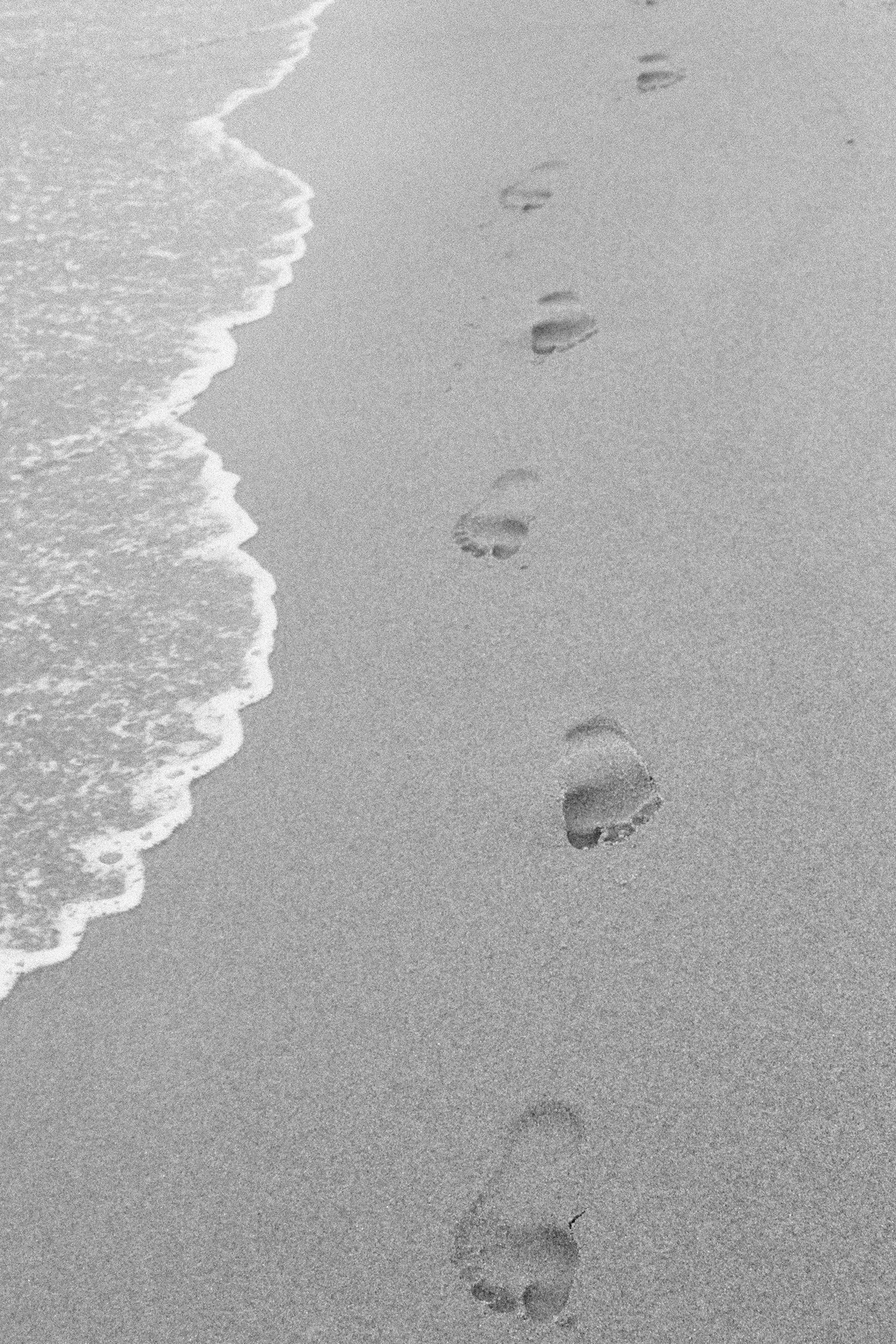 Footprints in the sand near the shoreline with small waves washing up.