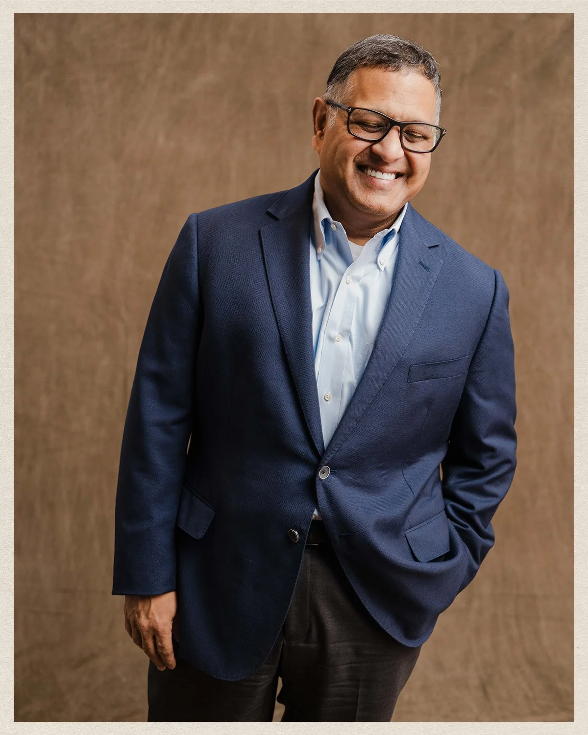 Neal Patel, A smiling man in a blue suit and white shirt standing against a neutral background.