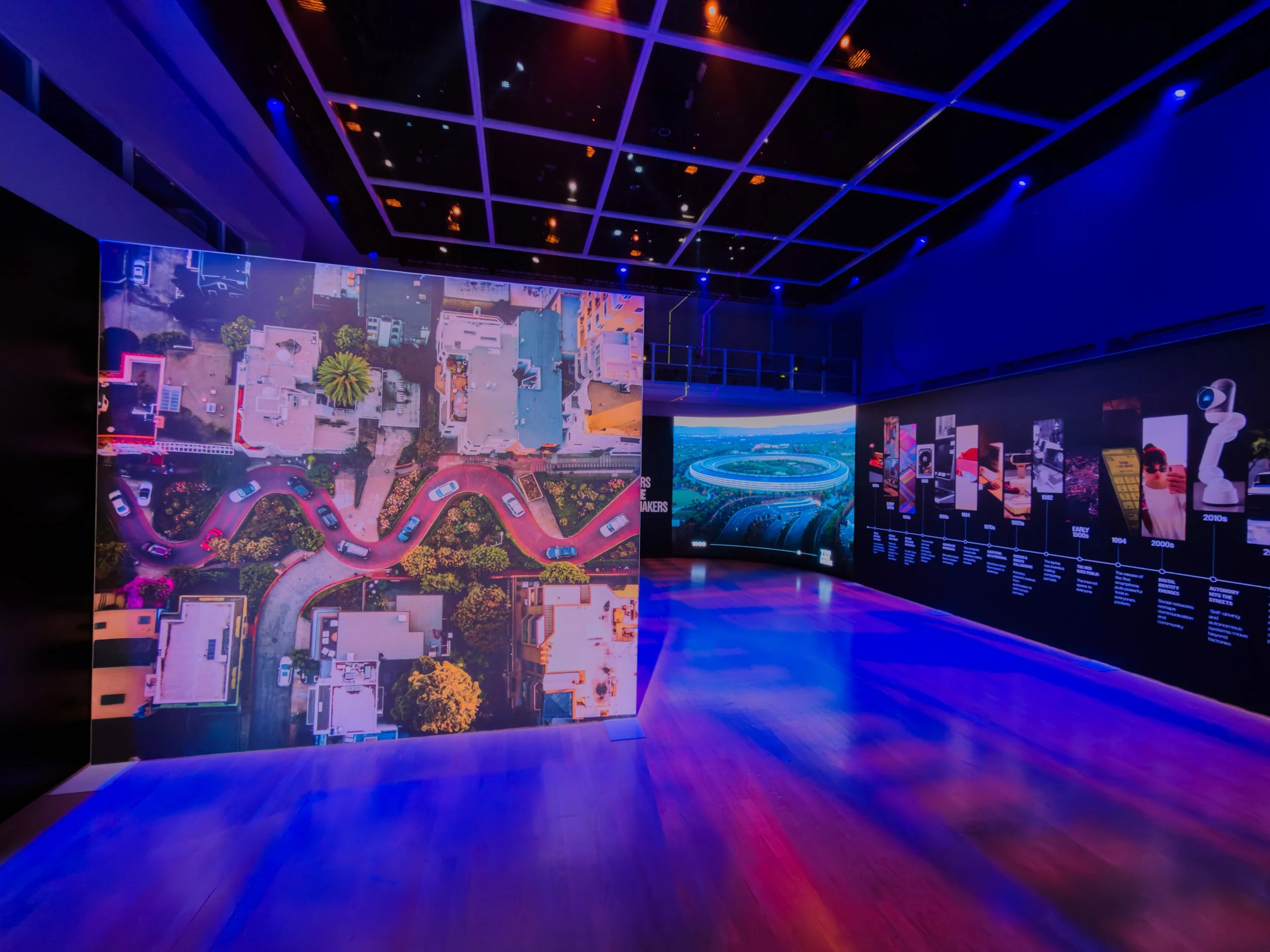 A dark room with large illuminated screens displaying cityscape images, surrounded by blue and orange lighting.