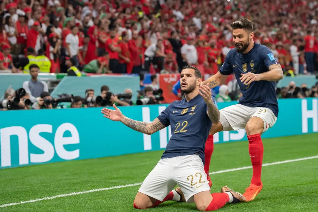 Two soccer players in blue jerseys celebrating a goal on a soccer field, with a large crowd of spectators in the background.