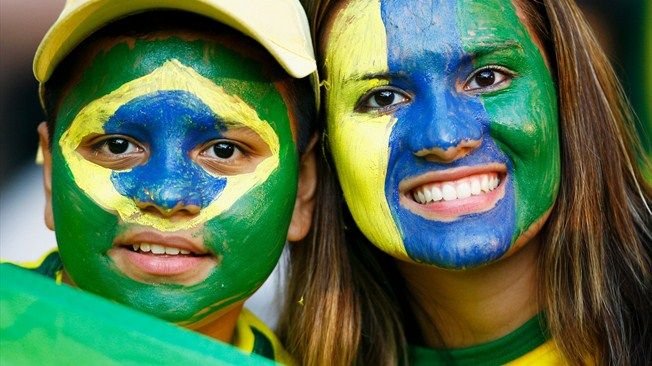 Two people with face paint in the colors of the Brazilian flag, smiling and close together.