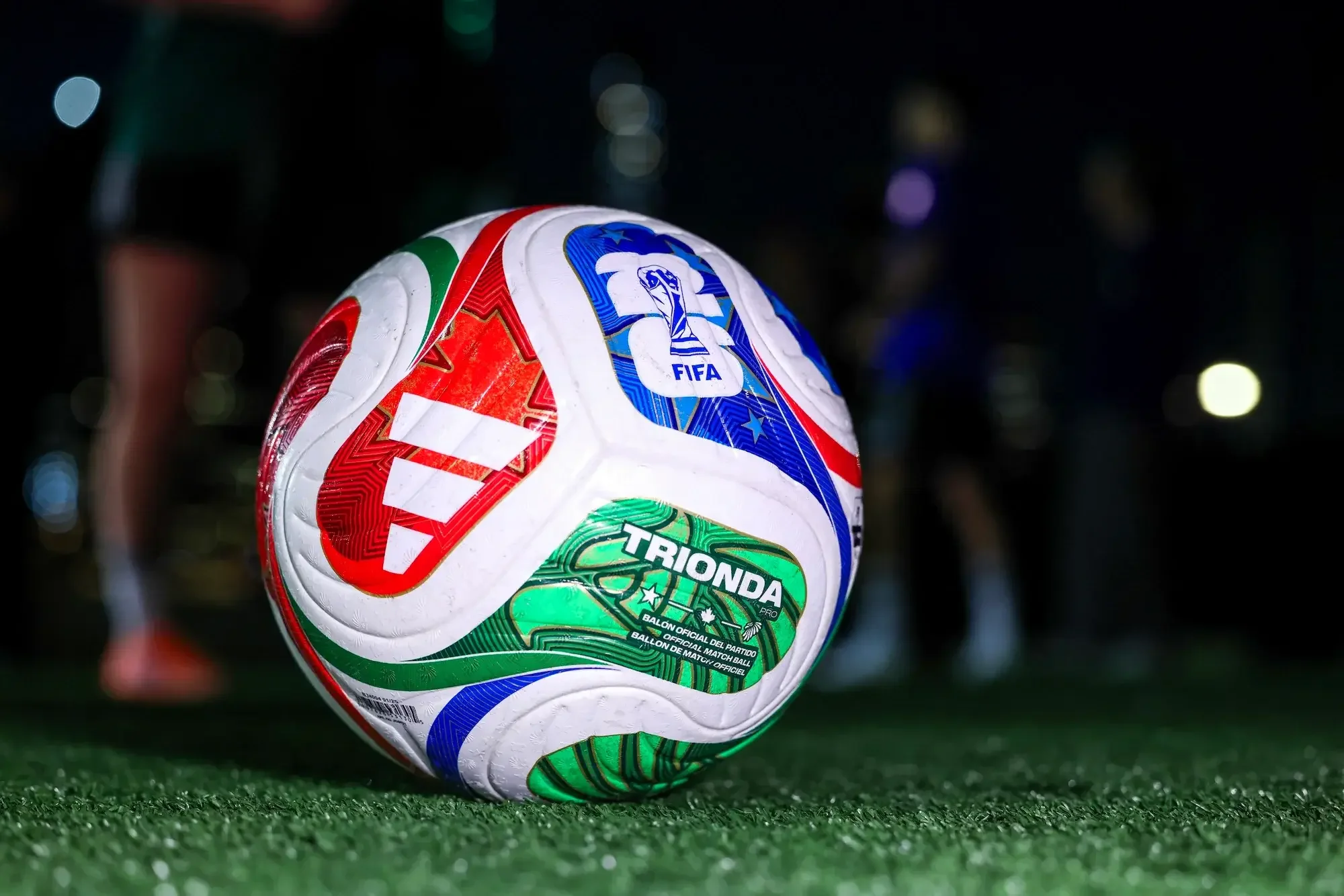 Colorful soccer ball on a green field at night with blurred background lights.