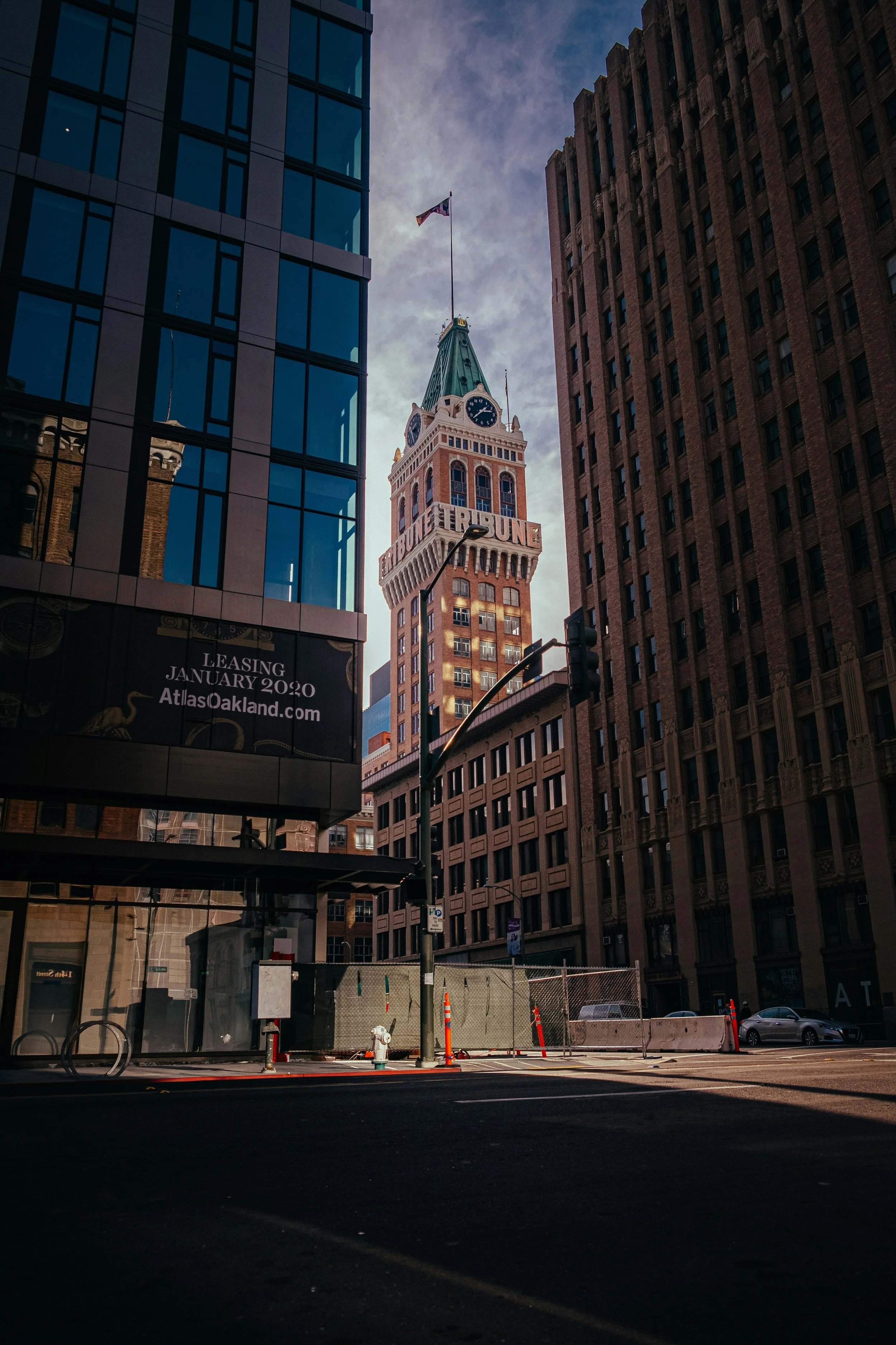 Downtown city street with the Ferry Building clock tower in San Francisco, framed by modern glass and older brick buildings, during daytime with cloudy sky.