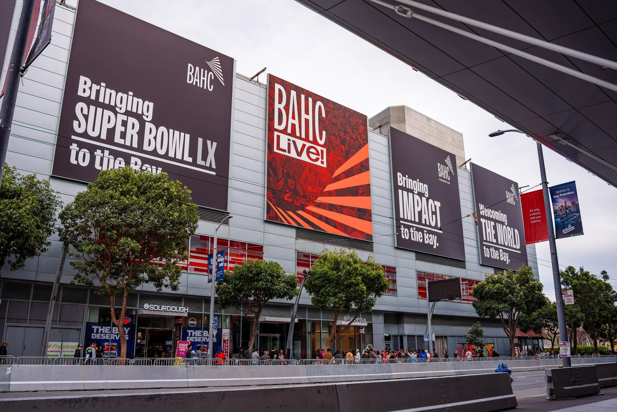 Exterior of the Chase Center in San Francisco, California, with large banners advertising the Golden State Warriors and upcoming events, and a crowd of people gathered outside the entrance.