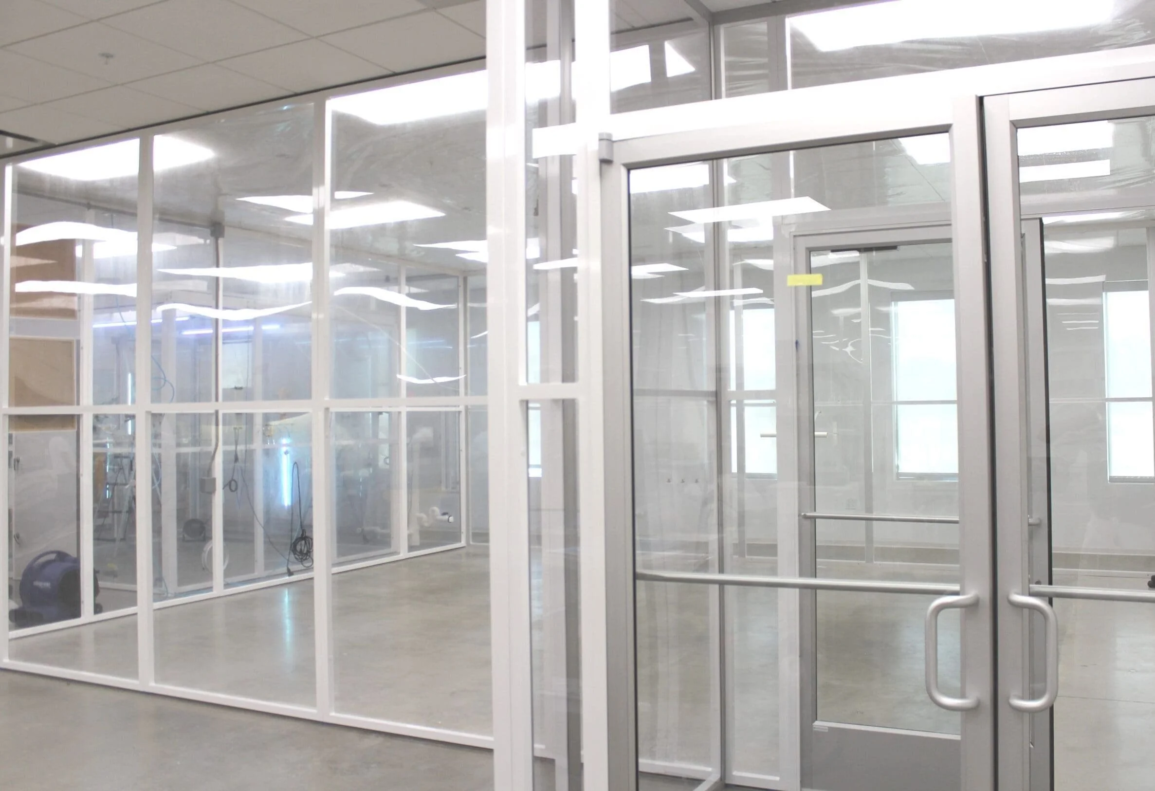 Empty office space under construction with glass walls and doors, construction equipment visible inside.