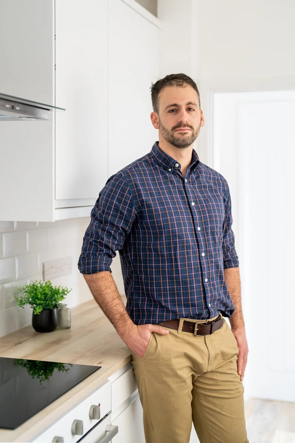 A man in a blue plaid shirt and khaki pants standing in a modern kitchen.