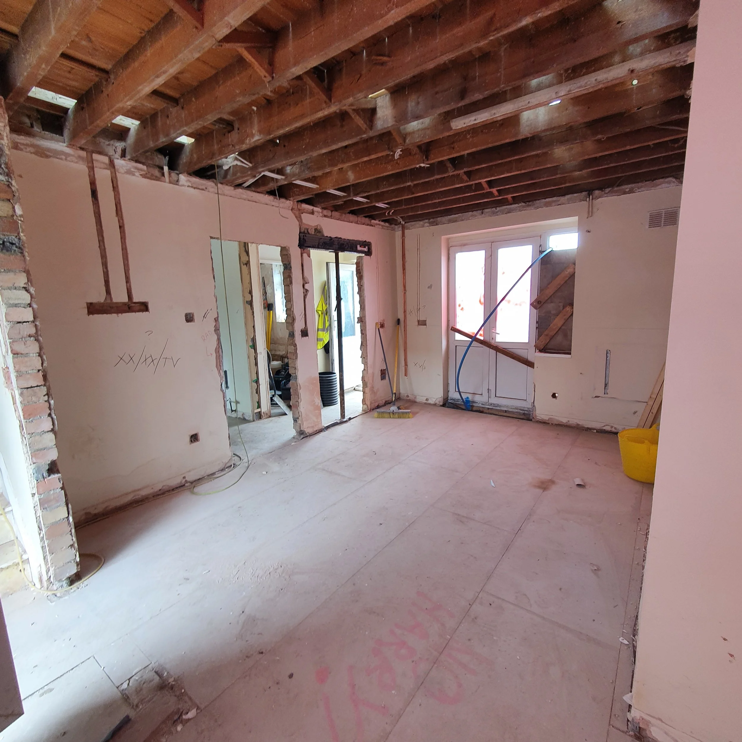 Interior room under renovation with exposed wooden ceiling beams, unfinished walls, and construction tools and materials.