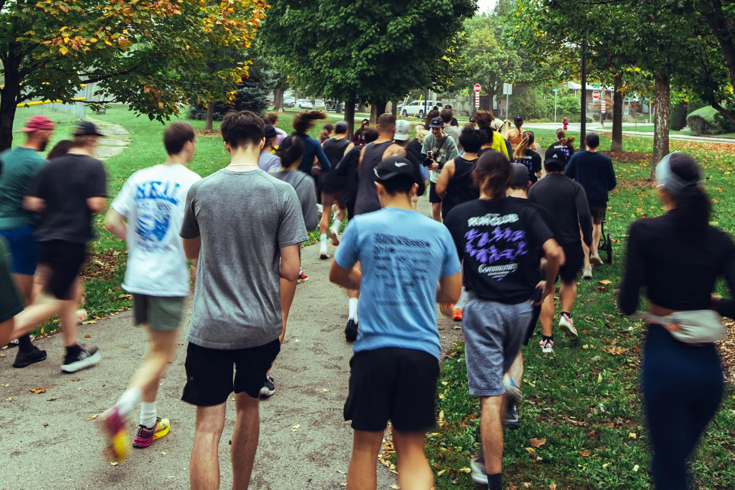 Group of people running or jogging outdoors on a park trail with trees and grass.