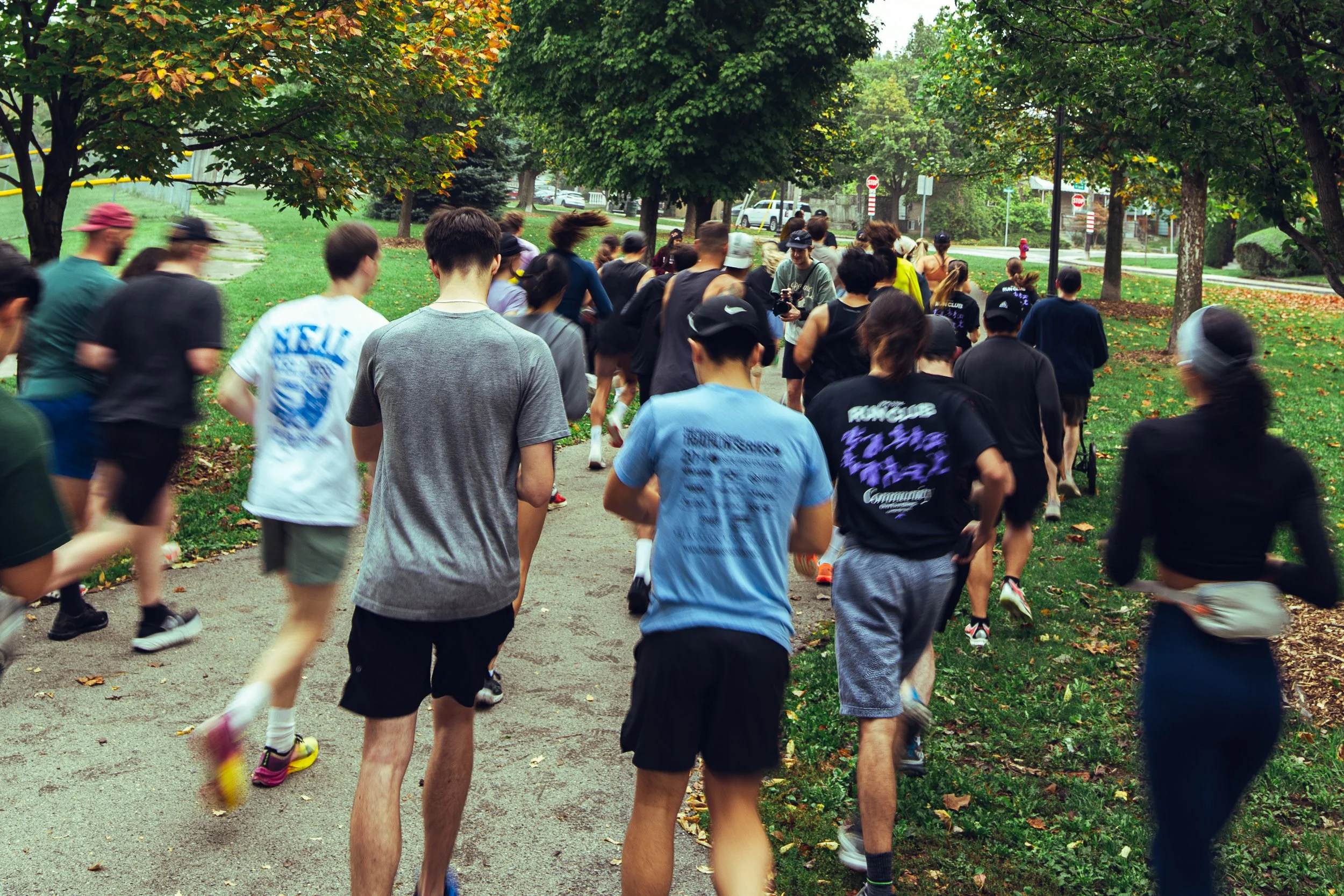 Group of people running or jogging outdoors on a park trail with trees and grass.
