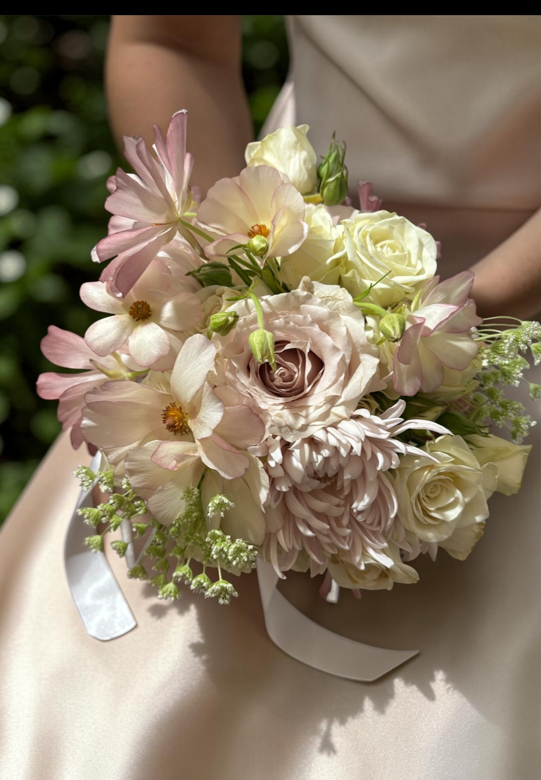 A bouquet of white and pink flowers including roses, dahlias, and other blooms, held by a person in a beige dress.
