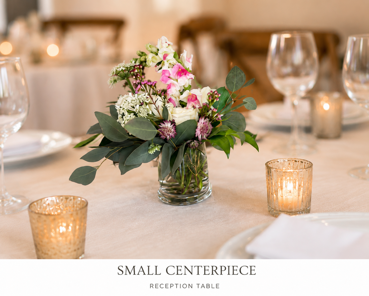 A small floral centerpiece with pink and white flowers and green leaves on a reception table, surrounded by glasses and candles.