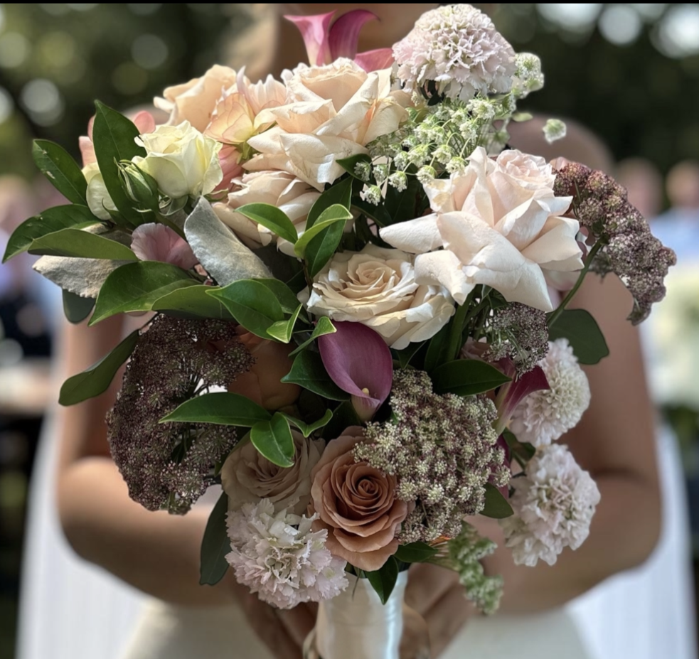 A person holding a large bouquet of various white, pink, and lavender flowers with greenery.