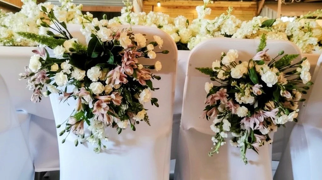 White chairs decorated with small bouquets of white and pink flowers at a wedding or event.