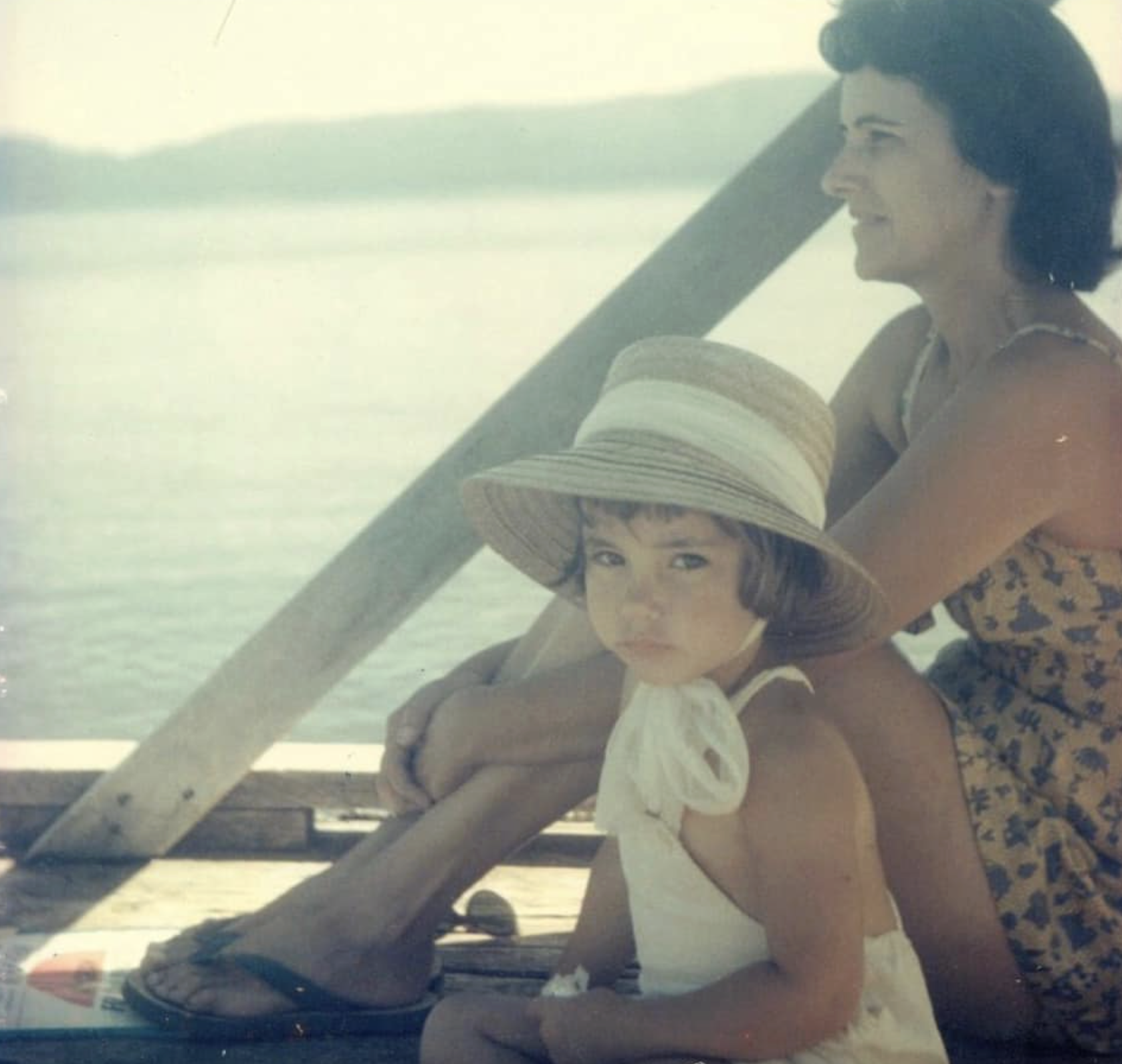 A woman and a young girl enjoying a boat ride on a lake, with both wearing summer clothing and the girl sporting a large straw hat.