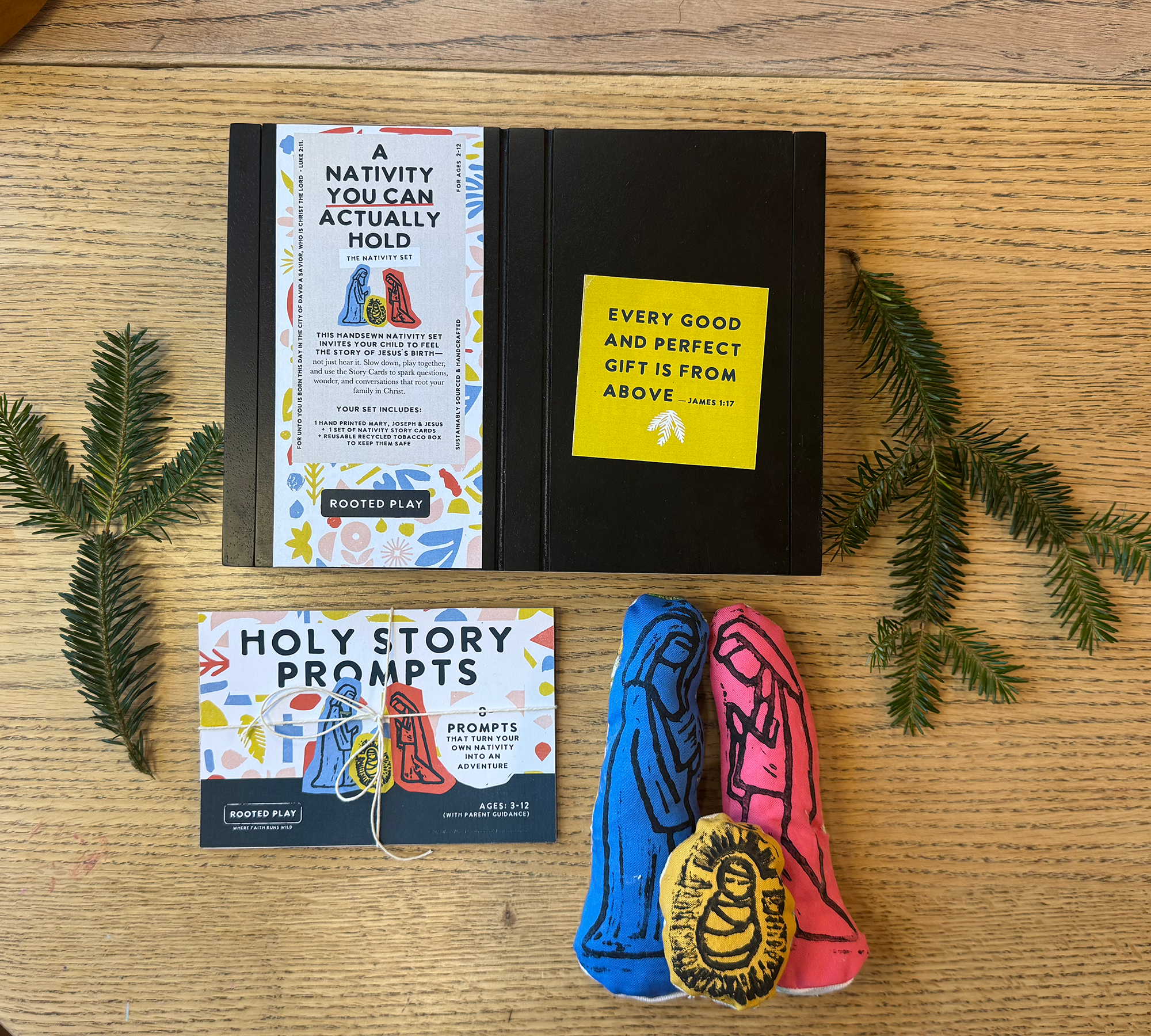 A nativity set and holy story prompts on a wooden surface, surrounded by pine branches.