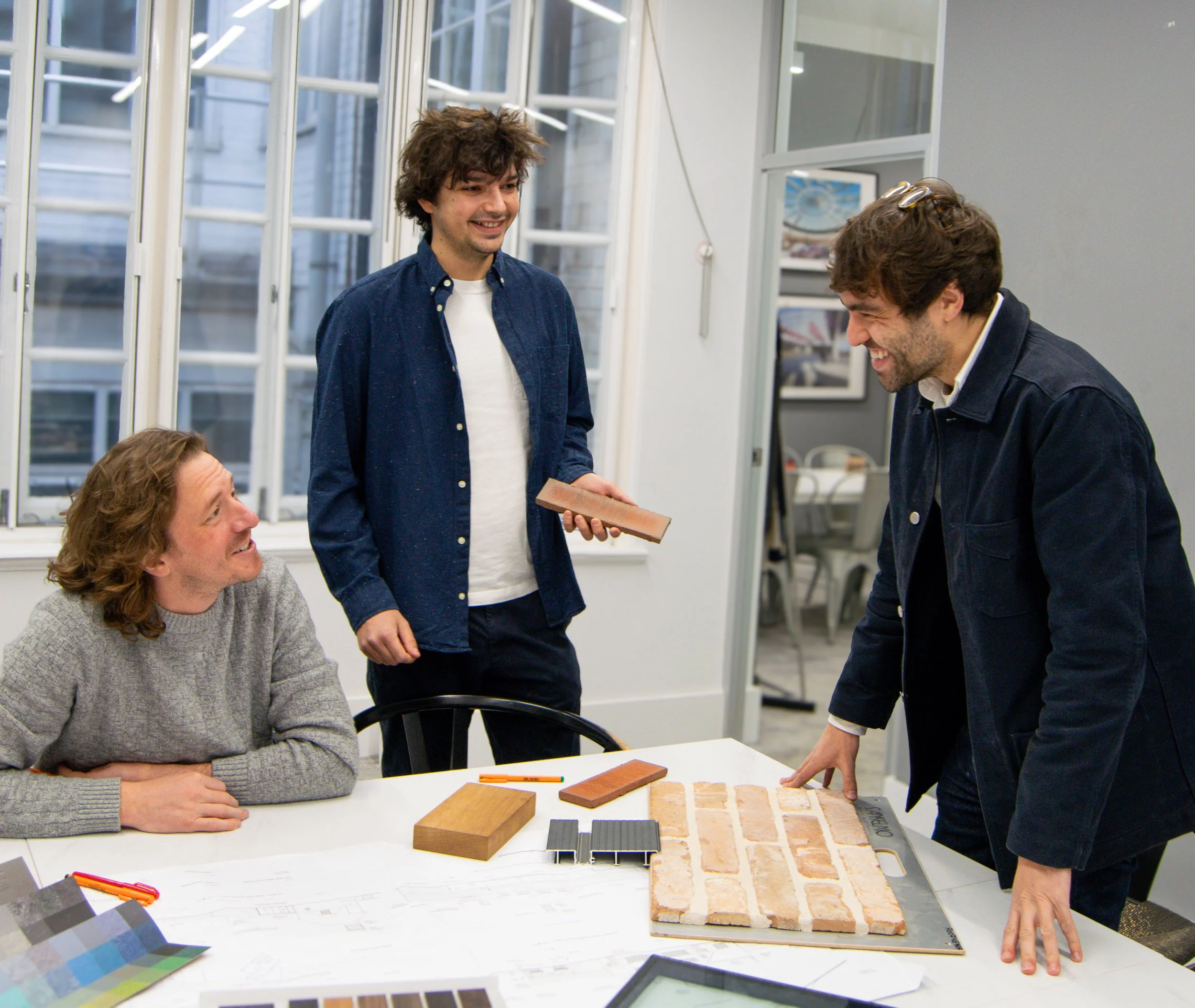 Bradley Roast, Dylan Warren, and Ryan Shedden in a meeting room discussing brick samples and color swatches.
