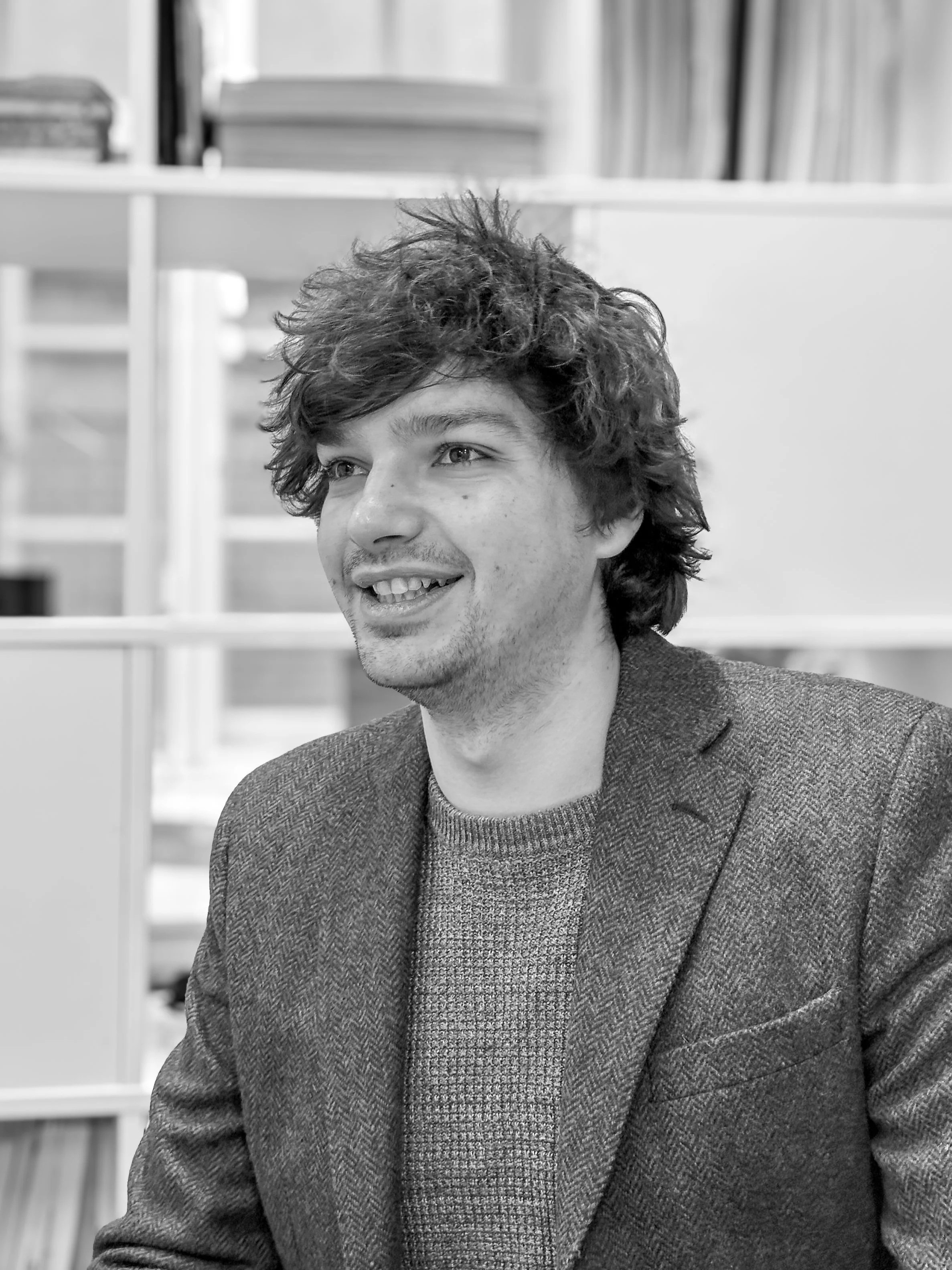 Dylan Warren sitting indoors with bookshelves in the background.