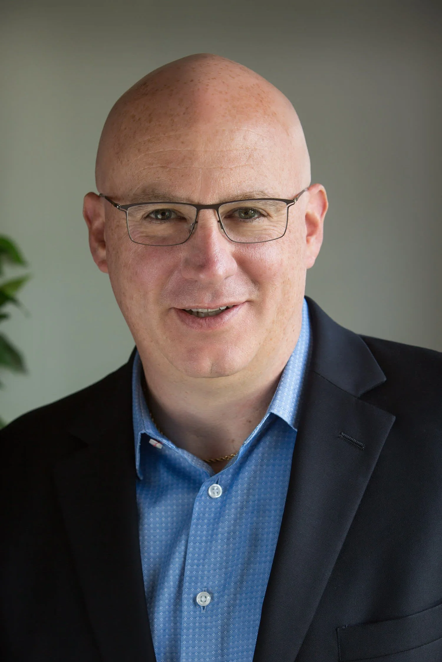A woman with long, light brown hair smiling, wearing a cream-colored top and a small cross necklace, against a dark blue background.