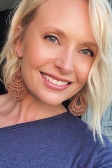 Blurry portrait of a person with short dark hair wearing a black top against a light background.