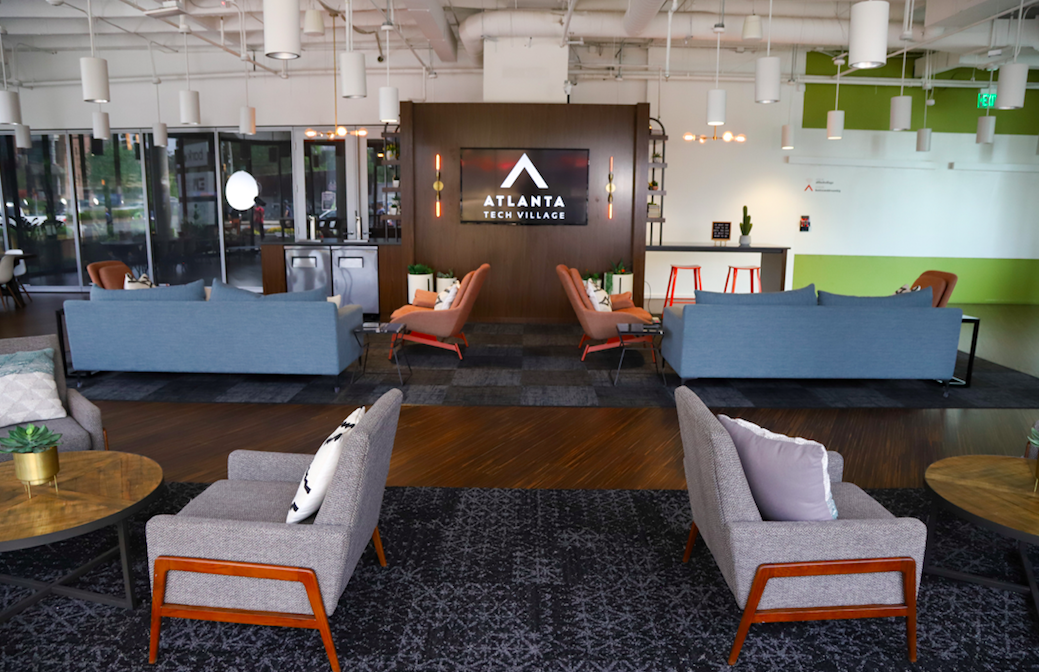Modern lobby of Atlanta Tech Village featuring sofas, armchairs, a reception desk, and a large screen displaying the Atlanta Tech Village logo.